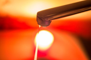 Yanan bir mumun arka planına karşı musluktan gelen ince bir su püskürtüsü. Savaş nedeniyle Ukrayna 'da elektrik ve su kesintileri