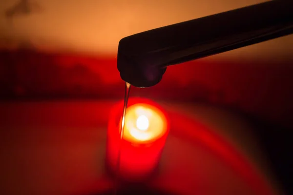 stock image A thin jet of water from a faucet against the background of a burning candle. Blackouts of electricity and water in Ukraine due to the war