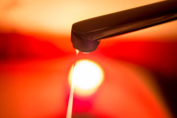 stock image A thin jet of water from a faucet against the background of a burning candle. Blackouts of electricity and water in Ukraine due to the war