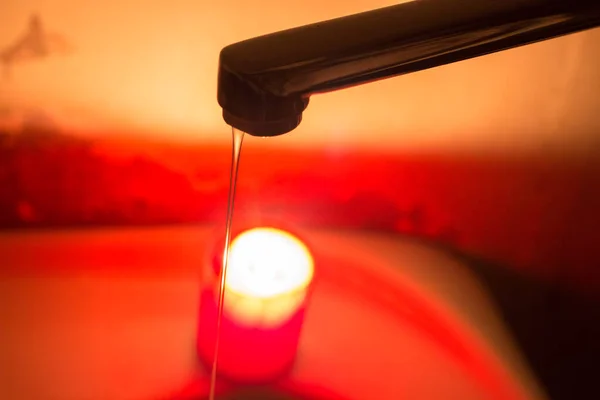 stock image A thin jet of water from a faucet against the background of a burning candle. Blackouts of electricity and water in Ukraine due to the war