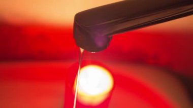 Yanan bir mumun arka planına karşı musluktan gelen ince bir su püskürtüsü. Savaş nedeniyle Ukrayna 'da elektrik ve su kesintileri