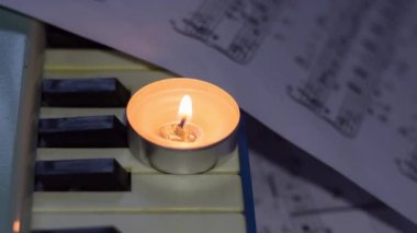 Çarşafların yanındaki sentezleyicinin tuşlarında yanan bir mum ve notalar. Ukrayna 'da savaş nedeniyle elektrik kesintisi
