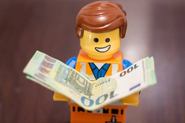 Slovakya. Sala. 1 / 01 / 2023 Euro banknotları bir LEGO işçisinin elinde, yüzünde neşeli bir ifadeyle... para Lego Film 2 Emmet Smile 'ın elinde.