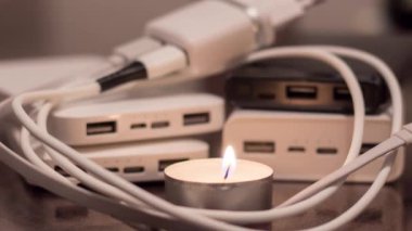 A burning candle against the background of power banks and a charger. Blackout due to war in Ukraine