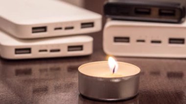 A burning candle against the background of power banks. Blackout due to war in Ukraine
