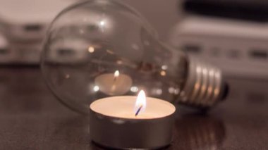 A burning candle against the background of a light bulb and power banks. Blackout due to war in Ukraine
