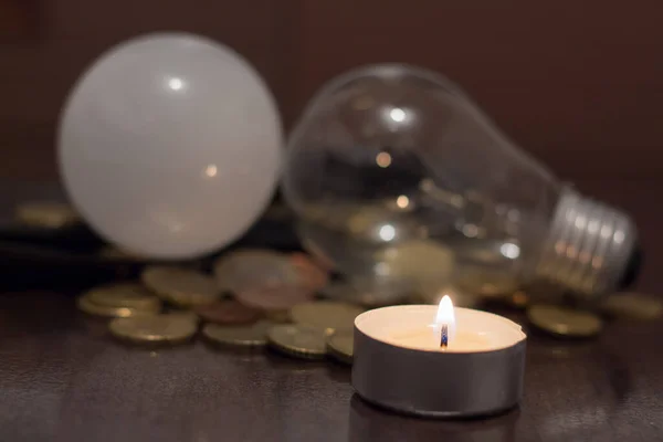 A burning candle and light bulbs t with money. Blackouts and rising electricity prices due to the war in Ukraine