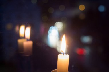 Reflection of a lit candle in the window glass in the evening. Power outages in homes due to the war in Ukraine.