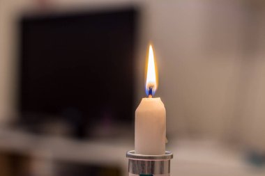 Burning candle on the background of the TV. Blackout due to war in Ukraine