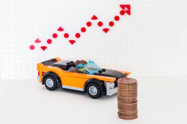 Lego car with coins on the background of sales growth arrows.