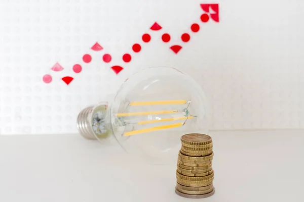 led light bulb with a column of coins on the background of a red growth arrow.