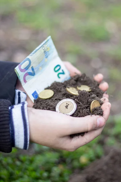 Money along with soil in the hands of a child.