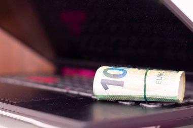 Bir dizüstü bilgisayarda yuvarlanmış euro banknotları.