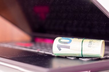 Bir dizüstü bilgisayarda yuvarlanmış euro banknotları.