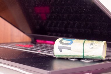 Bir dizüstü bilgisayarda yuvarlanmış euro banknotları.