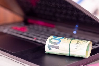 Bir dizüstü bilgisayarda yuvarlanmış euro banknotları.