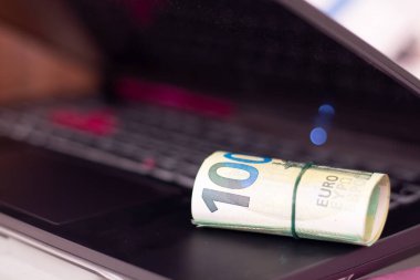 Bir dizüstü bilgisayarda yuvarlanmış euro banknotları.
