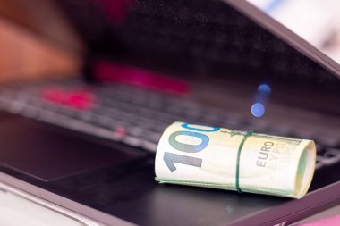 Bir dizüstü bilgisayarda yuvarlanmış euro banknotları.