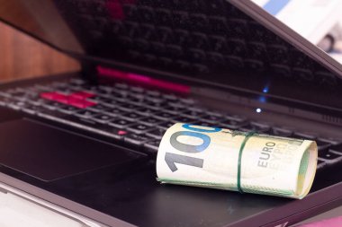 Bir dizüstü bilgisayarda yuvarlanmış euro banknotları.