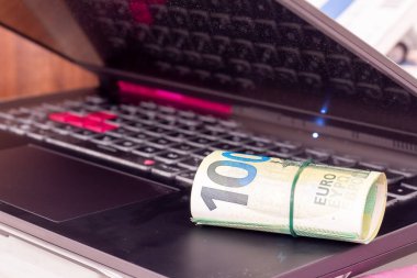 Bir dizüstü bilgisayarda yuvarlanmış euro banknotları.