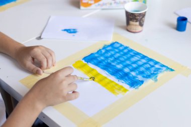 Çocuk bir kağıt parçasına boyalar çizer.