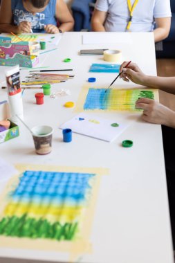 Çocuk bir kağıt parçasına boyalar çizer.