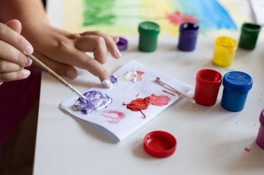 Çocuk bir kağıt parçasına boyalar çizer.