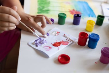 Çocuk bir kağıt parçasına boyalar çizer.