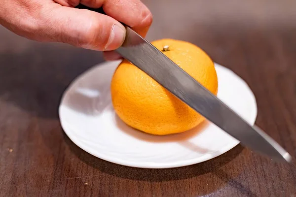 Slicing a tangerine with a knife in hand close-up
