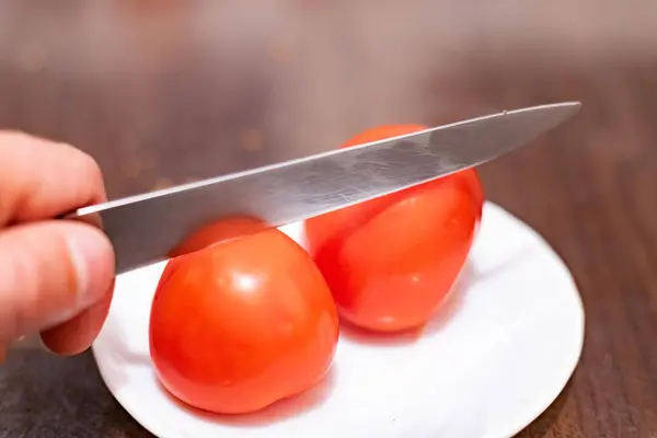 Slicing a tomato with a knife in hand close-up