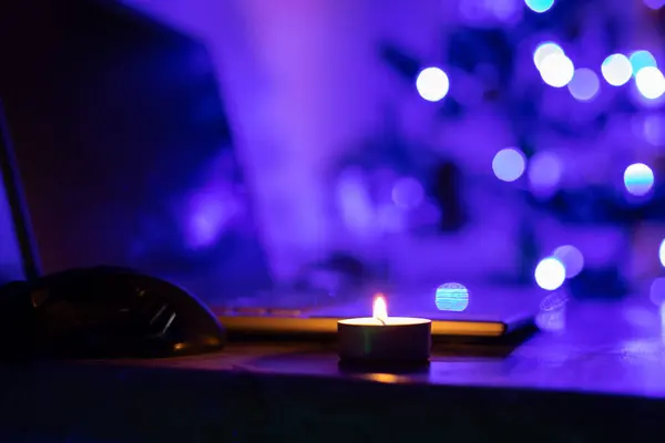 A burning candle on a laptop keyboard against the background of a New Year tree. Power outage due to war in Ukraine