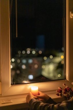 Bir çocuk pencerenin yanında yanan bir mum tutuyor. Ukrayna 'da savaş nedeniyle elektrik kesintisi