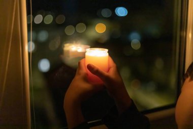Bir çocuk pencerenin yanında yanan bir mum tutuyor. Ukrayna 'da savaş nedeniyle elektrik kesintisi