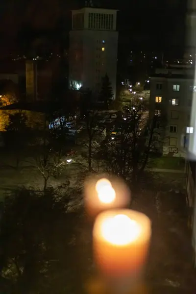 Burning candle near the window in the night city. Power outage due to war in Ukraine