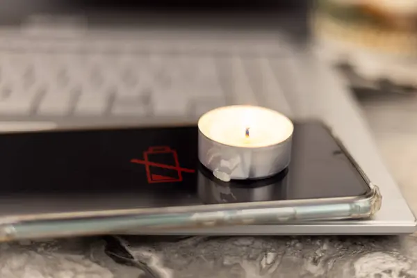 Burning candle on a discharged phone and laptop. Problems with electricity due to the war in Ukraine