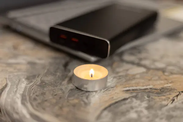 Burning candle near the power bank and laptop. Problems with electricity due to the war in Ukraine