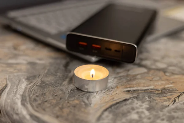 Burning candle near the power bank and laptop. Problems with electricity due to the war in Ukraine
