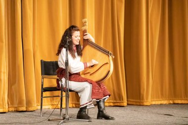 Ulusal kostümlü bir kız sahnede bandura çalıyor.