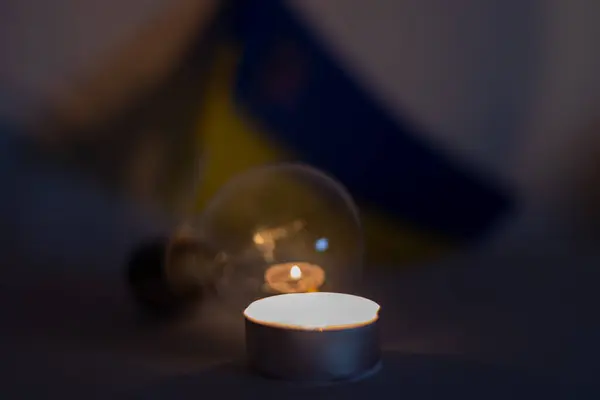 A burning candle and a non-working lamp on the background of the flag of Ukraine