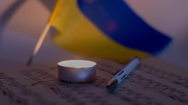 ウクライナの旗の背景にキャンドルと音楽シートを燃やす — ストック動画