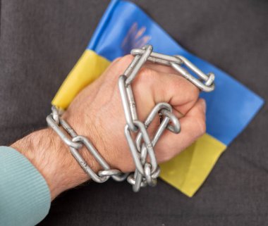 Bir adamın eli bir zincir ve Ukrayna bayrağına dolanmış. Ülkeden ayrılan vatandaşlara yasak