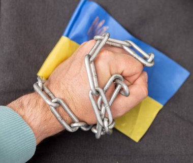 Bir adamın eli bir zincir ve Ukrayna bayrağına dolanmış. Ülkeden ayrılan vatandaşlara yasak