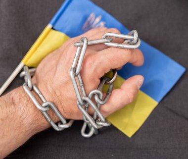 Bir adamın eli bir zincir ve Ukrayna bayrağına dolanmış. Ülkeden ayrılan vatandaşlara yasak