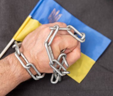 Bir adamın eli bir zincir ve Ukrayna bayrağına dolanmış. Ülkeden ayrılan vatandaşlara yasak