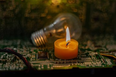 Akkor lamba ve elektronik devre kartlarının arka planında yanan bir mum. Ukrayna 'daki savaştan dolayı karartma