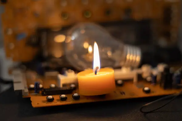 Akkor lamba ve elektronik devre kartlarının arka planında yanan bir mum. Ukrayna 'daki savaştan dolayı karartma
