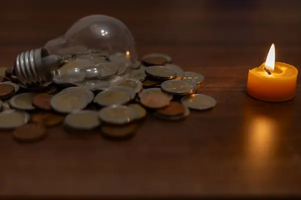 Stock image A lamp among coins and a burning candle. Rising electricity prices and blackout in Ukraine due to war