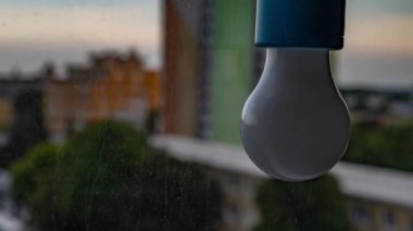 Pencerenin yanında bir ampul, bir akşam şehrinin arka planına karşı. Ukrayna 'daki savaştan dolayı elektrik yok.