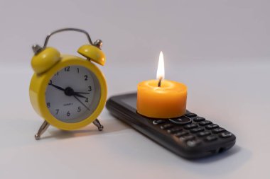 Burning candle on phone next to alarm clock. Power outage due to war in Ukraine clipart