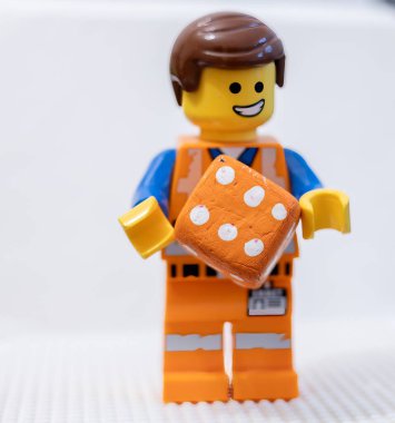 LEGO çalışanı, yüzünde neşeli bir ifadeyle, bir zar Lego Filmi 2 Emmet 'i tutuyor.